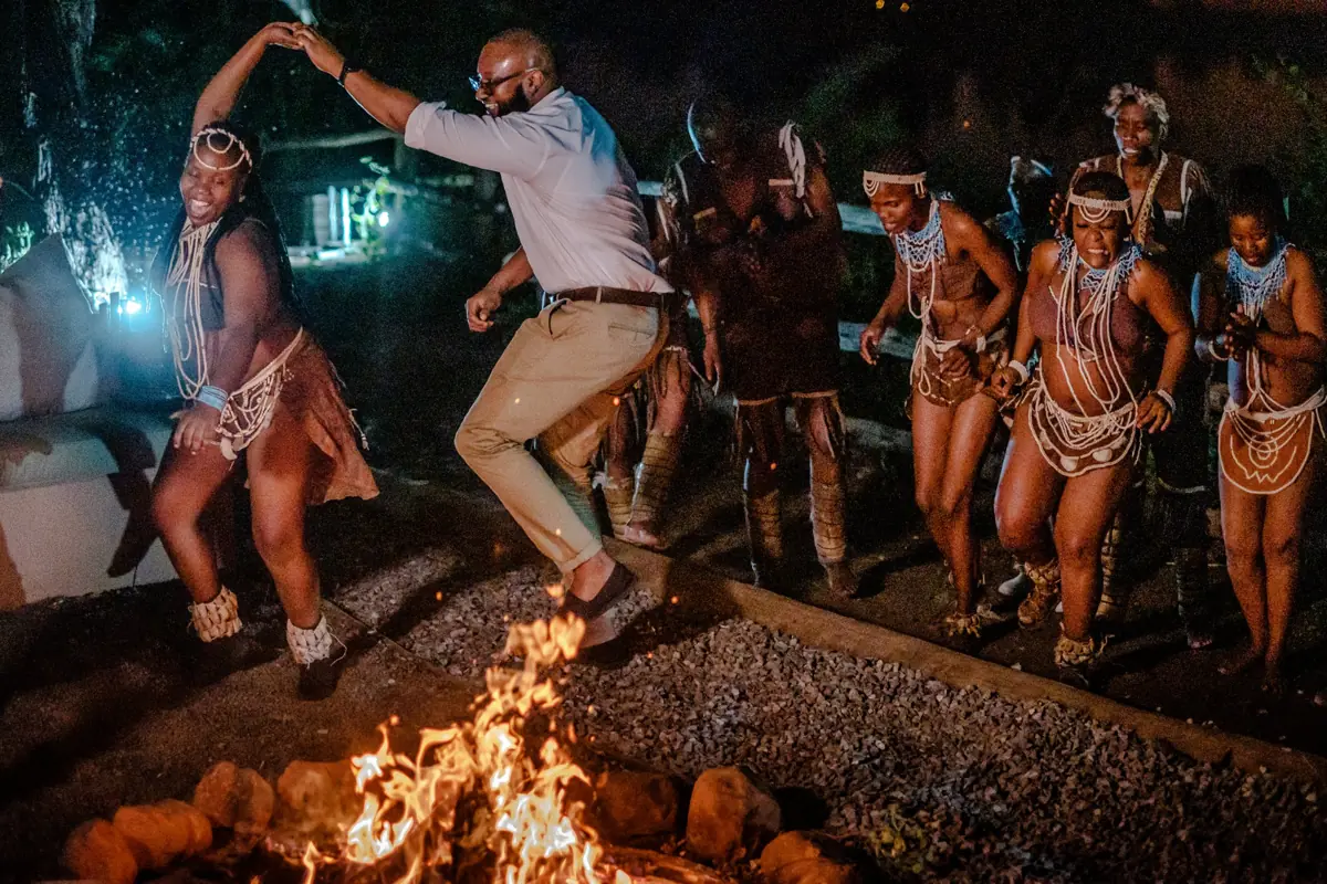 A guest dancing with traditional dancers beside the fire at night