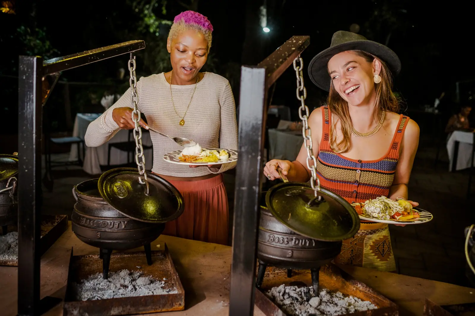 Guests serving themselves from cast-iron potjie pots over the coals at a potjie evening