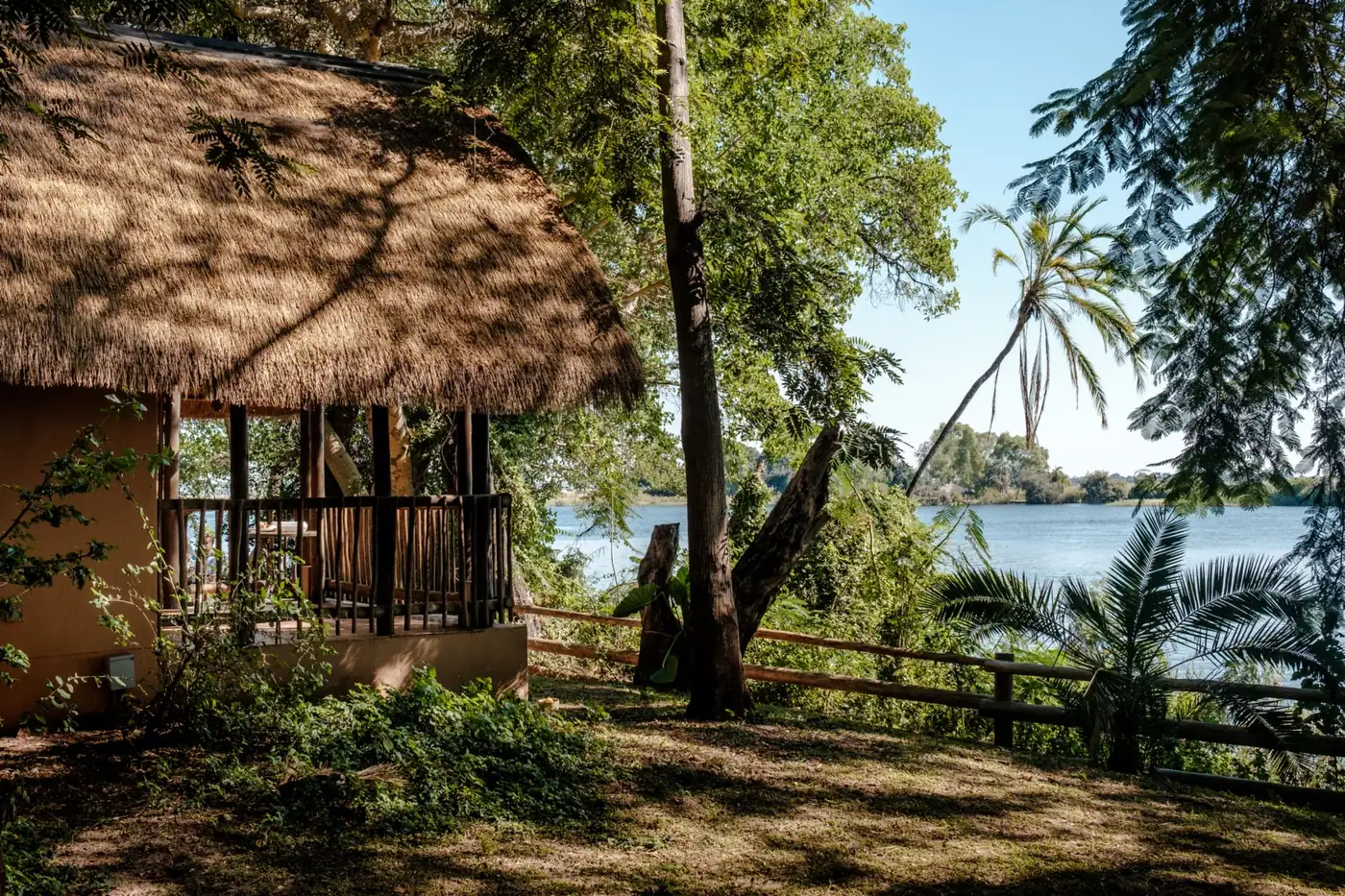 A thatched chalet with a timber veranda looking out over the river
